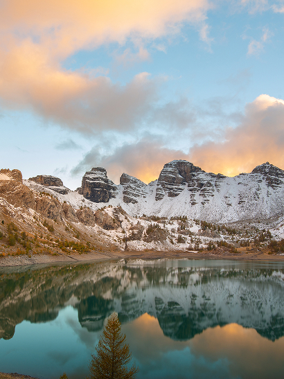 Lac alpin au coucher du soleil, montagnes enneigées reflétées dans l'eau